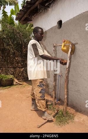 Man washes hands under self-made water tap from plastic container, Rwanda Stock Photo