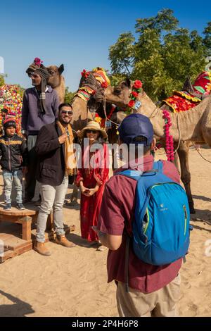 India, Rajasthan, Bikaner, Camel Festival, couple having souvenir photograph taken next to decorated camels Stock Photo