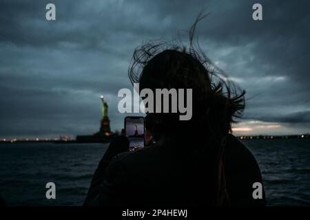 Woman taking a photo of Statue of Liberty on mobile phone Stock Photo