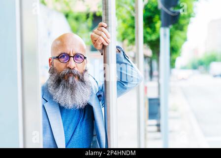 bald, bearded, bearded man standing leaning on bus stop pole Stock Photo