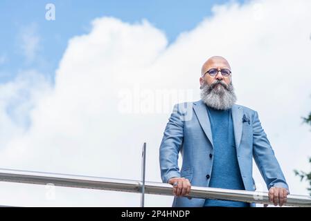 hipster man leaning on a fence looking at the camera Stock Photo
