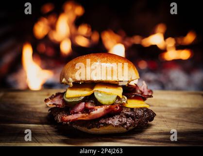 Smashed Cheeseburger on a wooden table in front of a fireplace. Stock Photo