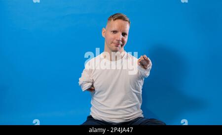 Hi Portrait of a friendly, joyful man with disabilities in a casual white T-shirt, showing a welcoming gesture, waving his hand and sincerely smiling Stock Photo