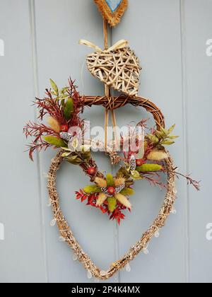A seasonal heart shaped wreath on a grey wood panelled door. Stock Photo