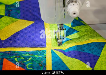 Closeup of detail of sewing machine with needle and on fabric sewn in pieces, bright handmade patchwork. Selective focus Stock Photo