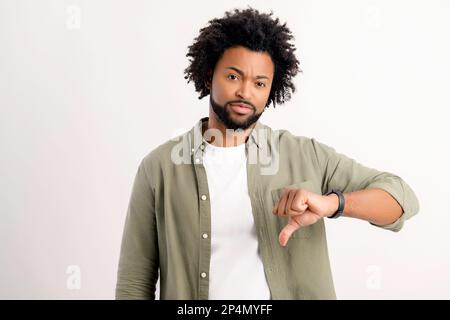 I do not like it. Serious unhappy African-American guy showing thumb down standing isolated on white, disagree with you, man in casual wear unsatisfied, discontent, uncontented Stock Photo