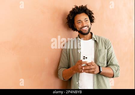 Carefree businessman using phone standing in modern office, cheerful friendly male employee texting online on mobile phone, chatting in social networks, web surfing Stock Photo