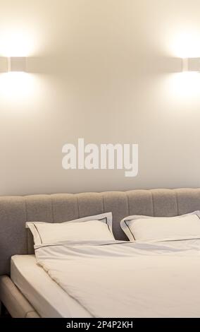 Double hotel bed with white bedding sheets and pillows on natural stone wall room background, messy bed concept Stock Photo