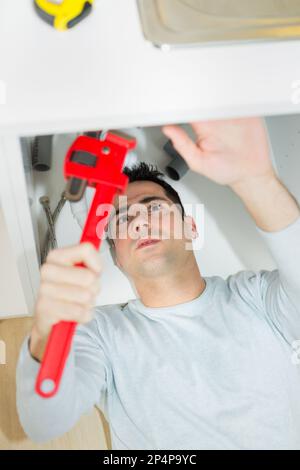 male plumber in overall fixing sink pipe Stock Photo