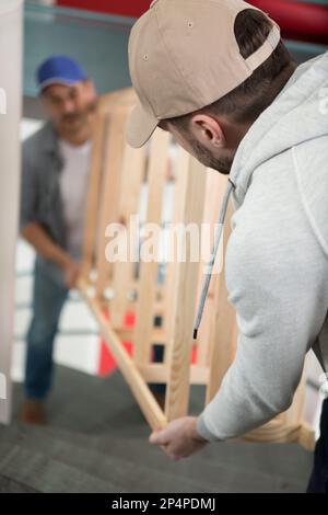 two male movers carrying the empty shelf on the staircase Stock Photo