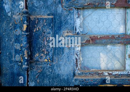 Cracked blue paint and reinforced widow on weathered old door. Stock Photo