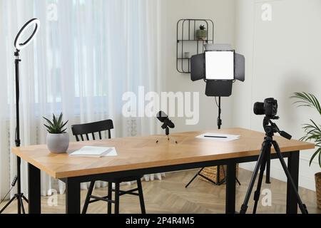 Camera and lighting equipment on tripods near table in room. Blogger workplace Stock Photo