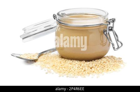 Tasty sesame paste in jar, spoon and seeds on white background Stock Photo