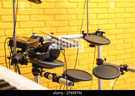 Modern electronic drum kit near yellow brick wall indoors. Musical instrument Stock Photo