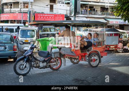 Motorcycle trailer taxi drivers sit in the back of a remork-moto, or tuk tuk, outside the Central Market in Phnom Penh while they wait for passengers. Stock Photo