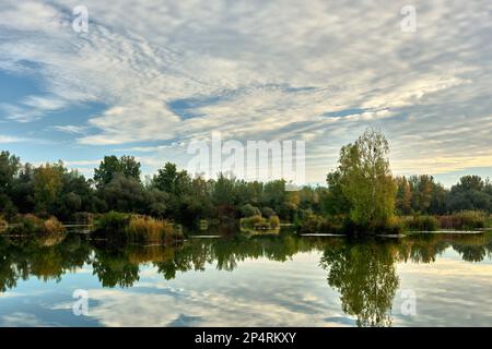 Lake with beautiful blue sky. Reflection of white puffy clouds in the calm water surface. Late autumn landscape. Early morning. Dubnica, Slovakia. Stock Photo