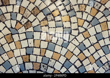 Vintage mosaic flooring fragment. Small squares in white, blue and yellow stone with black grout. Stock Photo
