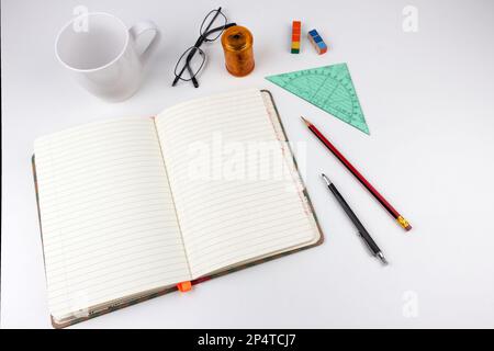 white table with paper notebook, a cup, pencil, glasses and other accessoires Stock Photo