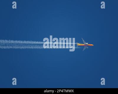 Tele close-up of a DHL cargo aircraft flying at high altitude in a clear blue sky with contrails Stock Photo