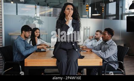 Pensive thinking female company CEO thoughtful businesswoman sitting on table office desk in boardroom think multicultural employees multiethnic Stock Photo