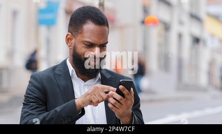 African American bearded man holding smartphone looking at mobile phone screen look for address with electronic online map app in city. Ethnic male Stock Photo