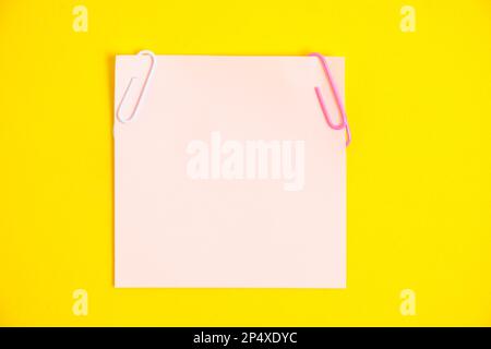 Pink sticker for notes and paper clips yellow background Stock Photo