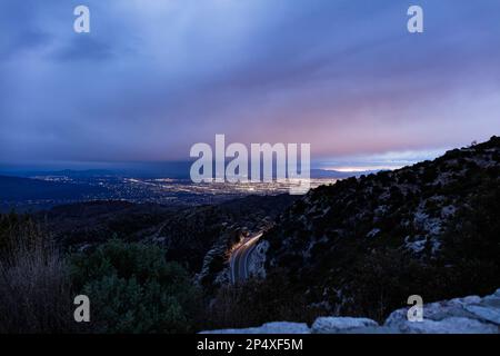 A nighttime view of Tucson, Arizona as seen from above in the Santa Catalina mountains. The headlights of a vehicle are seen moving down a mountain. Stock Photo
