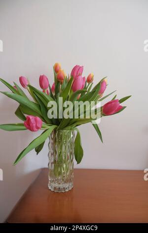 bouquet of pink and yellow tulips in vase closeup across white all on the wooden drawer. Interior detail. Hotel interior Stock Photo