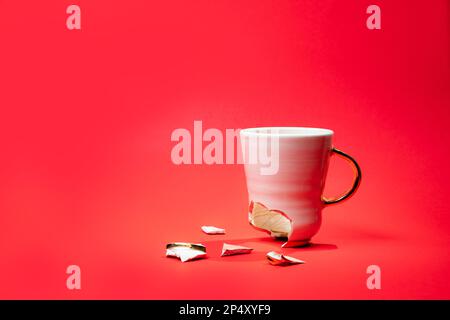 Broken tea cup isolated on red background. Cracked coffee mug and fragile ceramic pieces Stock Photo