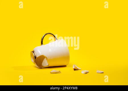 Broken tea cup isolated on yellow background. Cracked coffee mug and fragile ceramic pieces Stock Photo