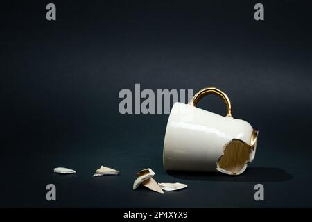 Broken tea cup isolated on black background. Cracked coffee mug and fragile ceramic pieces Stock Photo