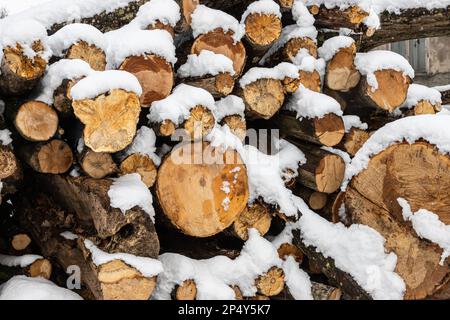 Snow covered firewood. Stack of wood cut. Snow on the timber stack. Wooden log store under snow. Stock Photo