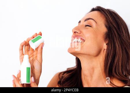 Beautiful laughing caucasian woman holding white mock up tube with green stikers in her hands. Young brunette female smiles with her eyes closed. Whit Stock Photo