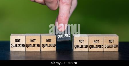 Symbol for finding a qualified candidate. Hand picks wooden cube with the text 'qualified' instead of cubes with the text 'not qualified'. Stock Photo