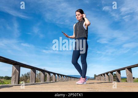 sportswoman adjusting her earphones during a workout break. Female runner listening to music on earphones during break outdoors. Stock Photo