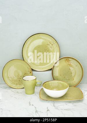 Set of green plates on white marble table with gray background. Collection of green dishware of different sizes on marble table Stock Photo
