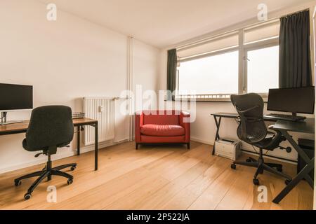 a living room with a red chair and computer on the desk in front of a large window that looks out onto the street Stock Photo