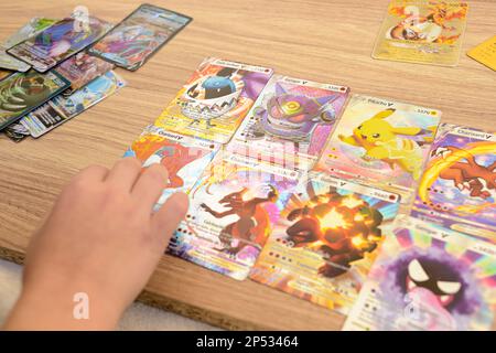 Arahal. Seville. Spain. 1st March 2023. Detail of a child's hands placing rare collectible Pokemon trading cards on a wooden table. Collectible tradin Stock Photo