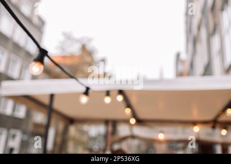 Blurred background, backyard illumination, light in the evening garden, electric lanterns with round diffuser. Lamp garland of light bulbs  Stock Photo