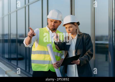 the architect shows the engineer the completed work. male and female talking near glass office Stock Photo