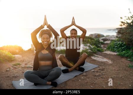 Smiling young african american lady and man in sportswear sit, enjoy workout, practice yoga in morning Stock Photo