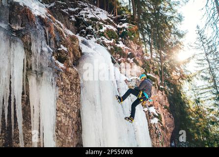 Ice climber dressed in warm winter climbing clothes, climbing harness and helmet abseiling frozen waterfall. Active people and sports activities conce Stock Photo