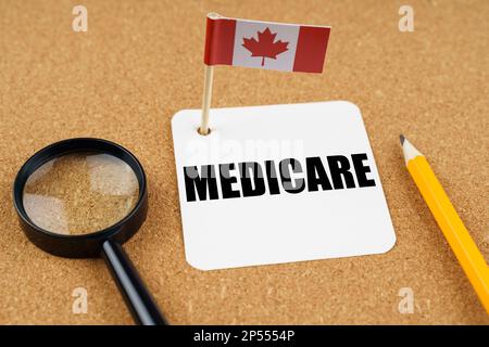 On the table is the flag of Canada, a pencil, a magnifying glass and a sheet of paper with the inscription - Medicare. Stock Photo