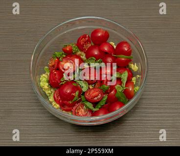 Healthy green salad with red cherry tomatoes in transparent glass bowl on kitchen table Stock Photo