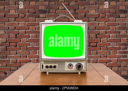 Vntage portable television with wood table, brick wall and chroma key green screen. Stock Photo