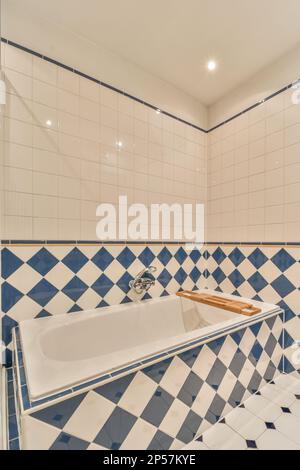 a tiled bathroom with blue and white tiles on the walls, along with a large bathtub in the corner Stock Photo