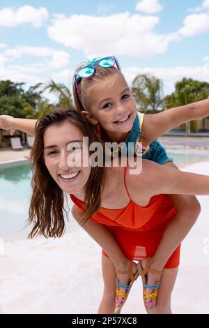 Portrait of happy biracial mother and daughter playing by the swimming pool Stock Photo