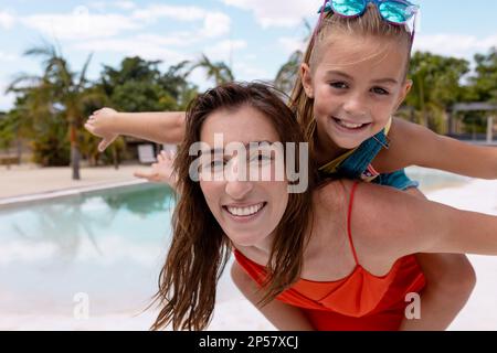 Portrait of happy biracial mother and daughter playing by the swimming pool Stock Photo