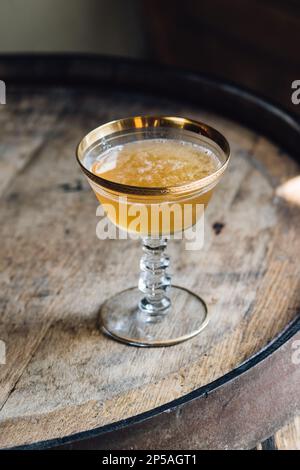 yellow whiskey cocktail in vintage hotel champagne coupe with gold rim sitting on barrel Stock Photo