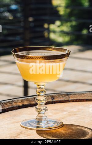 yellow whiskey cocktail in vintage hotel champagne coupe with gold rim sitting on barrel Stock Photo